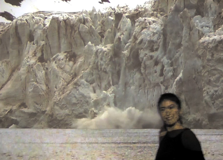 A viewer smiles at the camera as she walks in front of a video projection of a collapsing glacier
